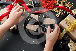 Christmas present stylish gift box in kids hands on black background. Creative Flat layout top view composition, banner, xmas, new