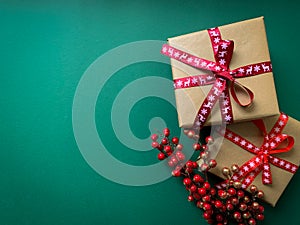 Christmas presents and branches of red berries laid on a green background. Flat lay with copy space.