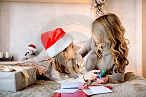 Christmas presents for children. in a bright guest house on the bed happy family mother and baby child daughter write a letter to