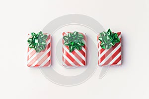 Christmas presents and new year gifts in red striped wrapping paper with green bows on white background with copy space.