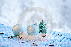 Christmas products background. Blue frosty pattern baubles on snow with green spruce tree shape candle burning.