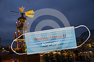 Christmas pyramid at night and a surgical face mask with German text Weihnachtsmarkt Abgesagt, meaning Advent Market cancelled,