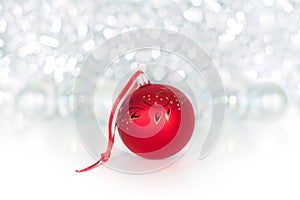 Christmas red ball on red ribbon on background of shiny tinsel, white bolls, lights and sparkles bokeh close up