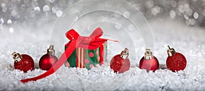Christmas red balls and gift box on snow, abstract bokeh lights background