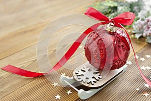 Christmas red bauble on sleigh with red ribbon bow, on wooden rustic table. Copy space