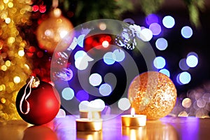 Christmas red and golden baubles with golden candles and tree sparking lights in background