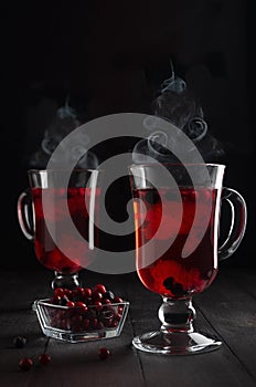 Christmas red hot mulled wine with berries and steam as Christmas tree shape in two transparent wine glasses on black wood table.
