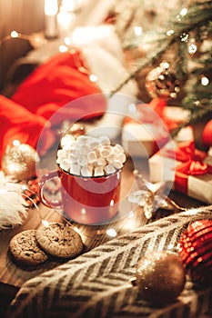 Christmas red mug with cocoa and marshmallows and cookies on a wooden table. New Year`s still life with a Christmas tree, a Santa