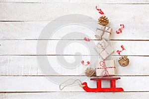 Christmas red sleigh driven by gift box, golden cones, streamers