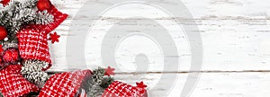 Christmas red and white corner border of ornaments, branches and ribbon on a white wood background