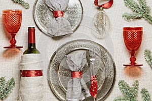 Christmas rustic table setting, red wine glass, plate, knife, fork, wine bottle, decorated green fir tree on sacking