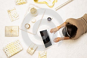 Christmas sale, discount. Online shopping. Woman using laptop for making order, buying gifts, lying on the snow-white carpet among