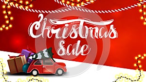Christmas sale, red discount banner with blurred background, garlands and red vintage car carrying Christmas tree