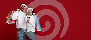 Christmas Sales. Couple In Santa Hats Holding Credit Card And Shopping Bags