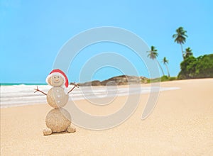 Christmas sandy snowman in santa hat at palm ocean beach