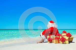Christmas Santa Claus with gift boxes relaxing at ocean beach
