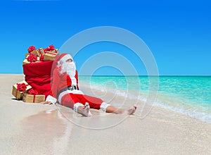 Christmas Santa Claus with gift boxes sack at tropical beach