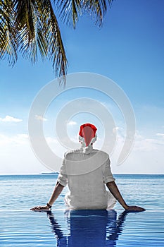 Christmas Santa Claus on the pool at the ocean sandy tropical beach. Santa Clause hat male model in the Maldives. Panorama banner
