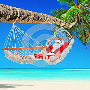 Christmas Santa Claus relax in hammock at tropical palm beach