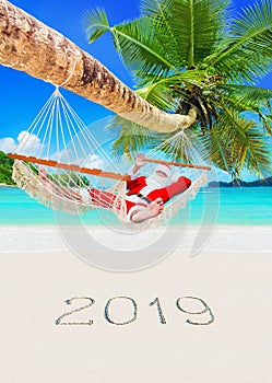 Christmas Santa Claus relax in hammock under palm at tropical sandy beach, season of happy new year 2019