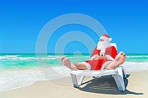 Christmas Santa Claus relax on sunlounger at ocean tropical beach