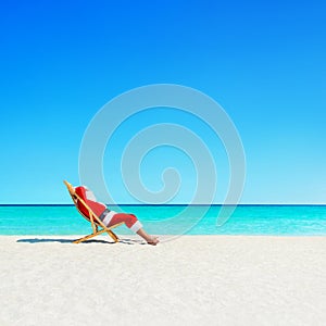 Christmas Santa Claus relaxing in sunlounger at ocean tropical b