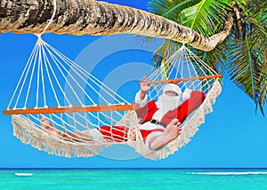 Christmas Santa Claus sunbathing in hammock at tropical palm beach