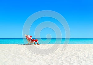 Christmas Santa Claus tan relaxing on sunlounger at sandy beach.