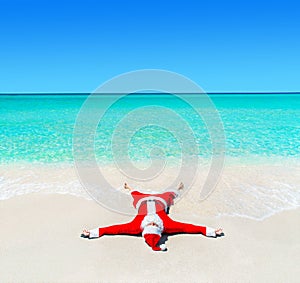 Christmas Santa Claus tanning at tropical ocean beach in waves