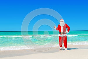 Christmas Santa Claus at tropical beach thumbs up hand gesture