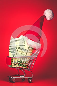 Christmas Santa hat on shopping cart full of money. Xmas cash gift, or chrismas spending concept