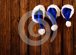Christmas Santa Hats hanging on Wooden Board Background. Xmas Family Claus Cap over brown Grunge Wood Plank Wall. Xmas Holiday