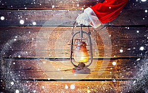 Christmas. Santa`s hand holding vintage oil lamp over wooden background
