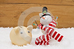 Christmas Savings, Piggy Bank and Snowman with scarf on snow wi