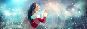 Christmas scene. Beauty brunette young woman in santa party costume blowing snow