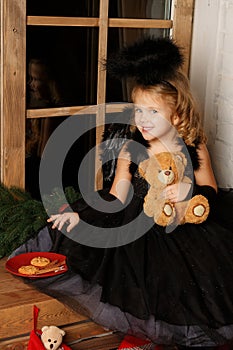 Christmas scene. portrait of a little blond girl, in a black angel costume stealing Santa`s cookies near the window.