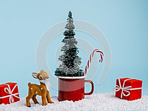 Christmas scene with red cup, pine tree, snow and small deer on pastel blue background. Creative Xmas or New Year festive concept.