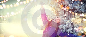 Christmas scene. Winter joyful beauty girl having fun outdoors in winter park under decorated Christmas tree