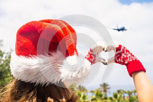 Christmas sea holiday. Back view of happy woman in santa claus hat and gloves showing heart shape from hand  and relaxing on parad