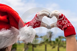 Christmas sea holiday. Back view of happy woman in santa claus hat and gloves showing heart shape from hand  and relaxing on parad