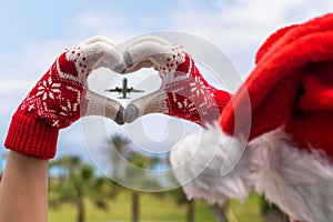 Christmas sea holiday. Back view of happy woman in santa claus hat and gloves showing heart shape from hand  and relaxing on parad