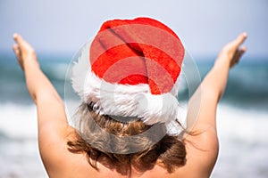 Christmas sea holiday. Back view of happy woman in santa hat showing thumb up and relaxing on paradise beach island getaway. New