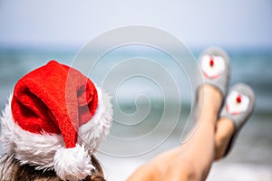Christmas sea holiday. Woman in santa claus hat and slippers relaxing on paradise beach island. New year.
