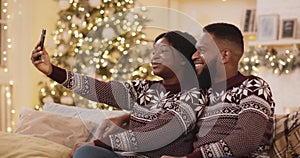 Christmas selfie. Young happy african american couple wearing winter sweaters making photo near Xmas tree at home