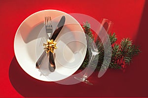 Christmas served dinner, table design on red background. White plate, champagne glass, fir, gold bow, fork, knife. New year