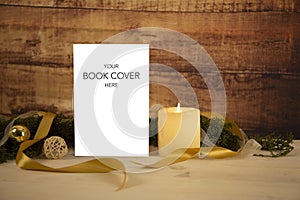 Christmas setting for a book presentation: book with blank cover settled with three lit candles , white organza and gold satin