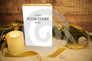 Christmas setting for a book presentation: book with blank cover settled with three lit candles , white organza and gold satin