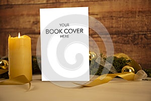 Christmas setting for a book presentation: book with blank cover settled with three lit candles , white organza and gold satin