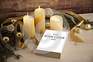 Christmas setting for a book presentation: book with blank cover settled with three lit candles , white organza and gold satin