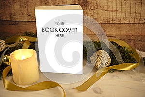 Christmas setting for a book presentation: book with blank cover settled with three lit candles , white organza and gold satin